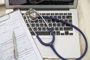 Geöffneter Laptop mit Stethoskop auf der Tastatur  und Formular
